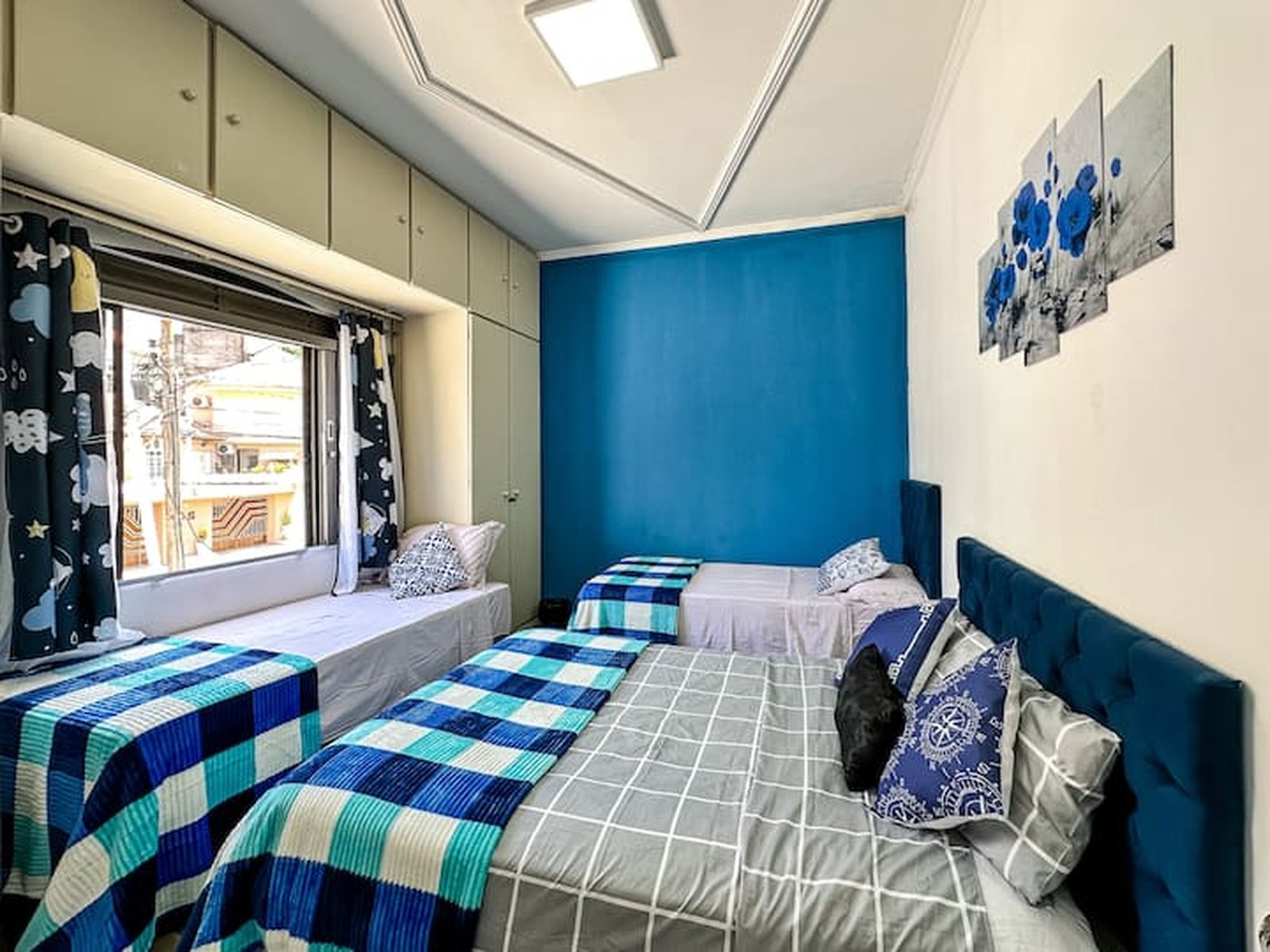 Quarto azul com três camas e vista para a rua