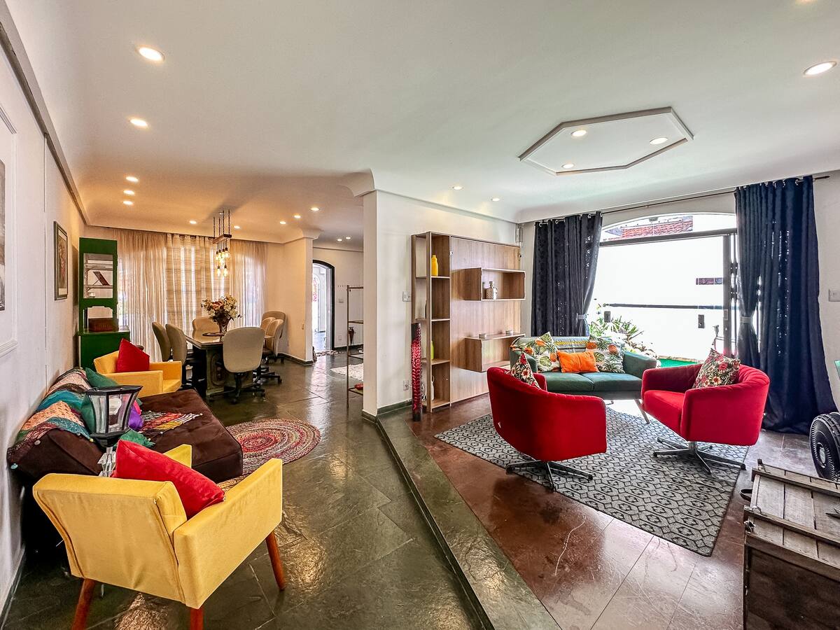 Sala ampla de uma das casas, com poltronas coloridas, sofá e mesa de jantar ao fundo